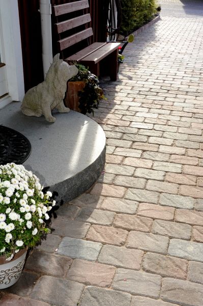 grå trappsteg utanför villadörr med marksten, bänk, vita blommor och hundstaty